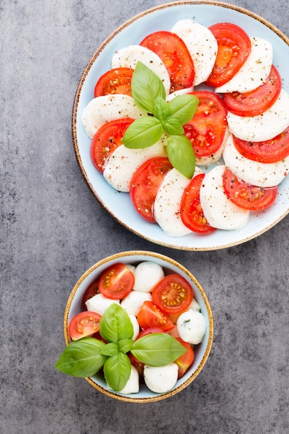 Tomaten, Mozzarella, Basilikum und Gewürze auf grauer Schiefersteintafel. Italienische traditionelle Caprese-Salatzutaten. Mediterranes Essen.