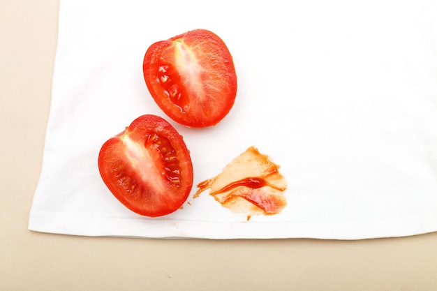 Tomaten und Ketchupfleck auf weißer Hemdkleidung auf beigem Hintergrund