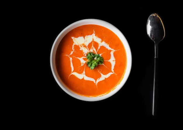 Tomatencremesuppe auf schwarzem Hintergrund mit Löffel