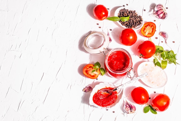 Tomatenkonfitüre, Marmelade, Chutney, Sauce im Glas. Hausgemachtes Erhaltungskonzept. Frische Tomaten, Gewürze, Knoblauch, Gemüse, Meersalz. Modernes hartes Licht, dunkler Schatten, weißer Kitthintergrund, Draufsicht