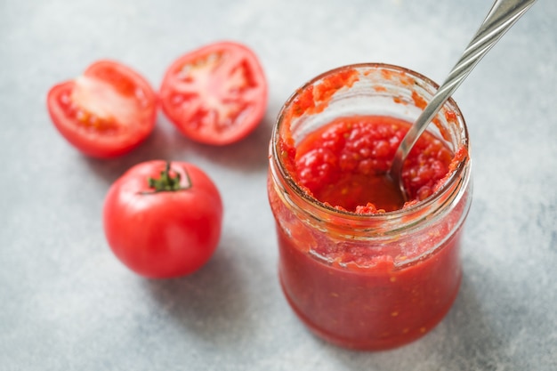 Tomatenmark eingemacht in einem Glasgefäß und in frischen Tomaten auf einem konkreten Hintergrund. Fermentation von Produkten.