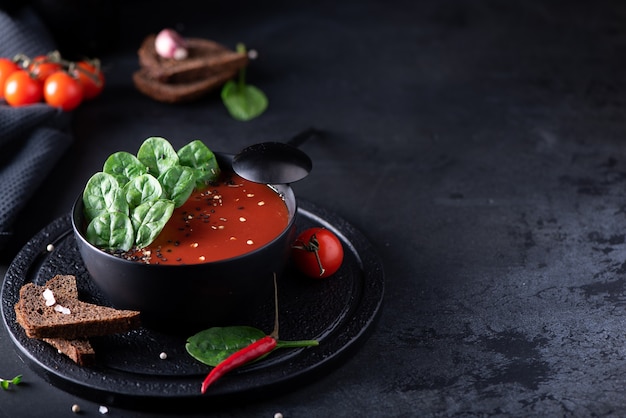 Tomatenpüreesuppe mit Spinat in einer schwarzen Schüssel, Nahaufnahme