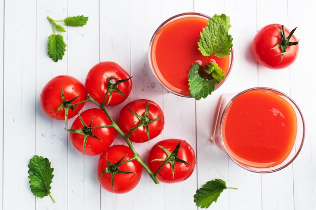 Tomatensaft in Glasgläsern und frischen reifen Tomaten auf einem Zweig. Weißer hölzerner Hintergrund mit.