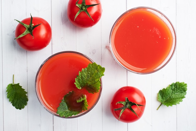 Tomatensaft in Glasgläsern und frischen reifen Tomaten auf einem Zweig. Weißer hölzerner Hintergrund mit.