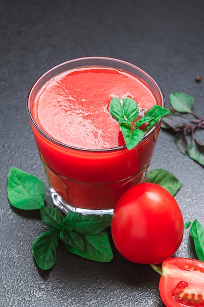 Tomatensaft mit Gewürzen, die Basilikum auf einem schwarzen Tisch würzen