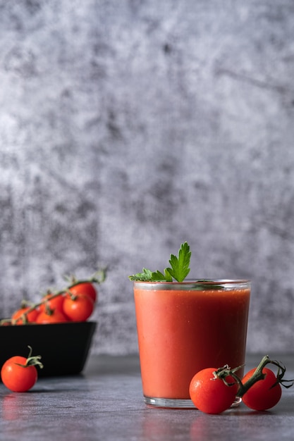 Tomatensaft, Tomatensaft in ein Glas gießen, Tomatensaft spritzen, auf grauem Hintergrund