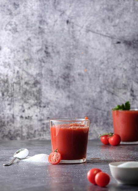 Tomatensaft, Tomatensaft in ein Glas gießen, Tomatensaft spritzen, auf grauem Hintergrund