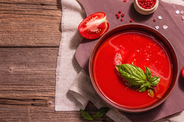 Tomatensuppe mit Basilikum in einer Schüssel. Reifes Gemüse, frisches Grün, duftende Gewürze. Vintage Holztisch, Ansicht von oben