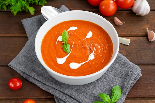 Tomatensuppenpüree in einer Schüssel mit Sahne und frischen Basilikumblättern auf dunklem Holzhintergrund Kopierbereich