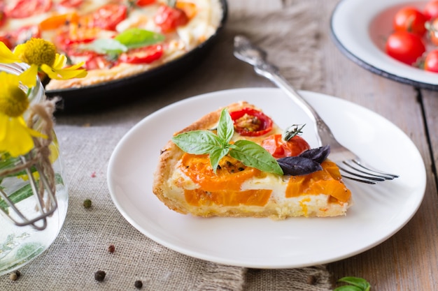 Tomatentarte mit Mürbeteig, roten und gelben Tomaten, Käse und Sahne. Konzept der gesunden Ernährung oder des vegetarischen Lebensmittels auf rustikalem hölzernem Hintergrund