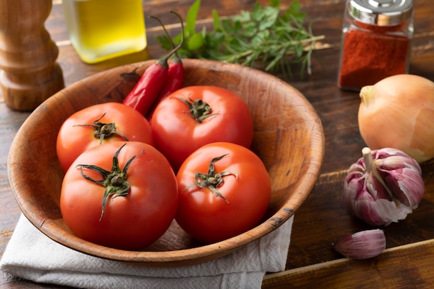 Tomates, ajos, pimientos y hierbas sobre mesa de madera.