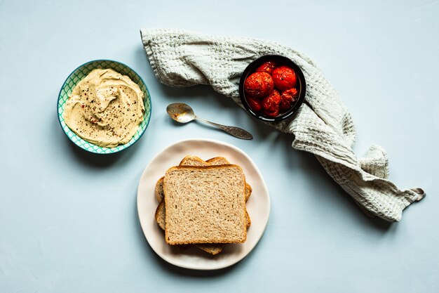 Tomates al horno, hummus y pan. Una toalla beige y una cuchara. Superficie azul. Vista superior de la imagen horizontal.