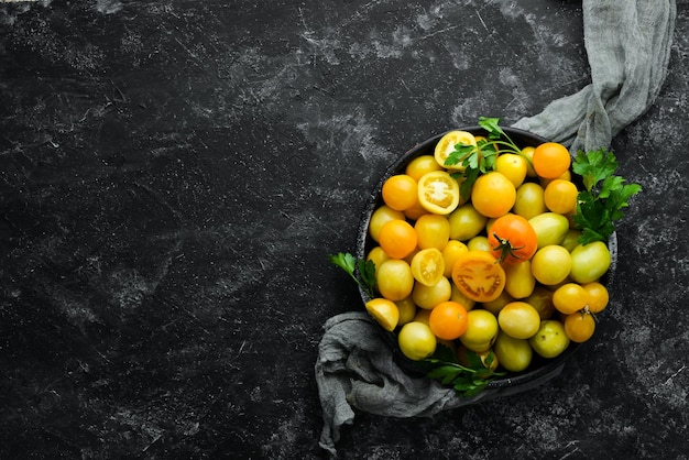 Tomates amarelos em uma tigela preta sobre um fundo de pedra preta Vista superior Espaço livre para o seu texto