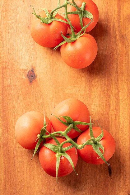 Tomates belos detalhes de tomates vermelhos frescos em galhos sobre a vista superior de madeira rústica