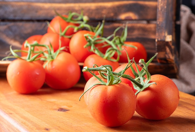 Tomates belos detalhes de tomates vermelhos frescos em galhos sobre foco seletivo de madeira rústica