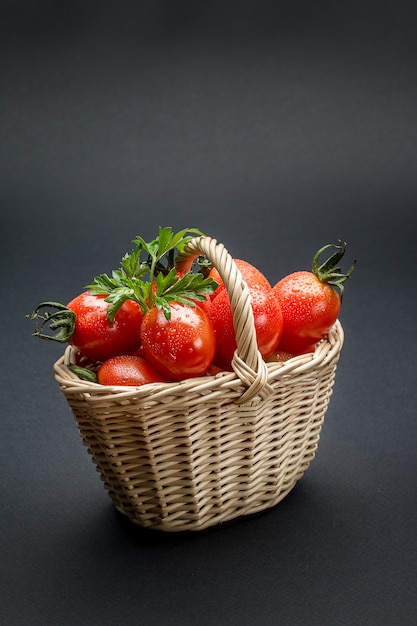 Tomates en una canasta de mimbre sobre superficie gris