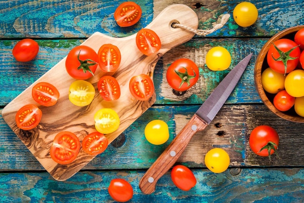 Tomates cereja amarelos e vermelhos cortados em uma tábua na mesa velha