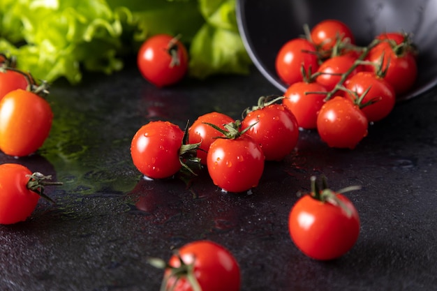 Tomates cereja caíram do prato. fundo escuro decorado com folhas de salada