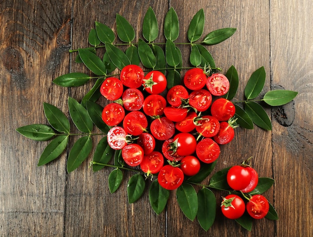 Tomates cereja dispostos em forma de coração com folhas verdes sobre fundo de madeira