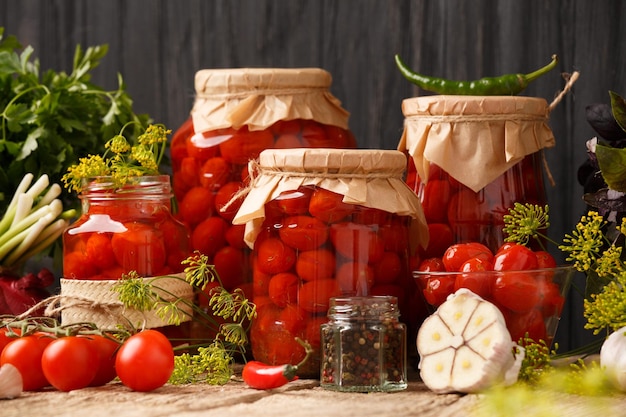 Tomates cereja enlatados em frascos fechados, especiarias e ervas para marinada sobre fundo de madeira rústica