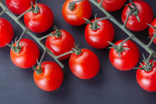 Tomates cereja maduros em um galho em um fundo escuro de madeira Espaço de cópia de vista superior