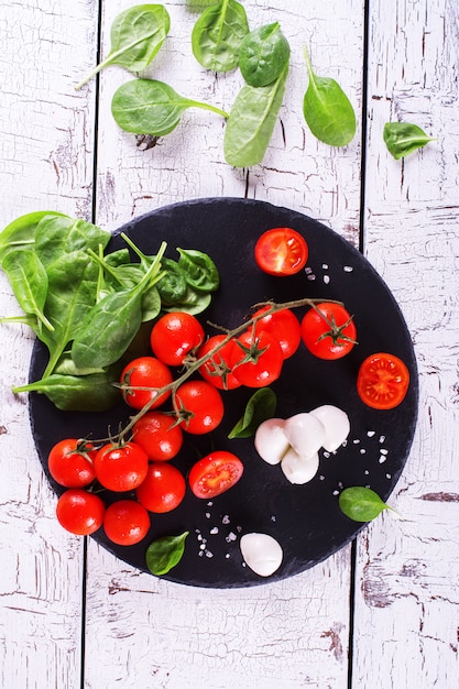 Tomates de cereza frescos, mozzarella y espinaca verde en fondo de madera.