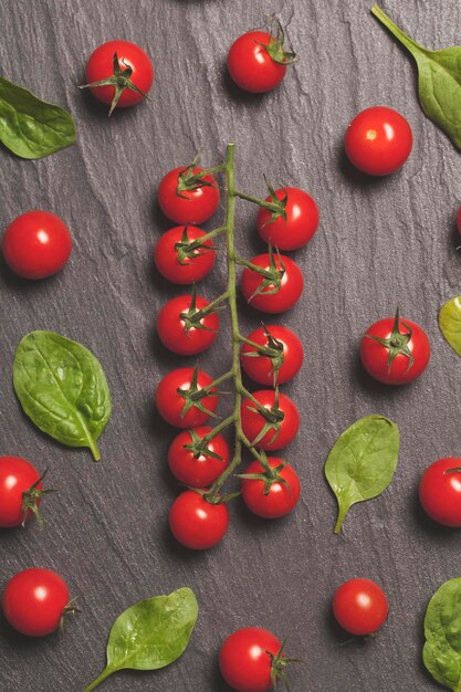 Foto tomates de cereza roja y hojas de ensalada verde sobre un fondo de pizarra