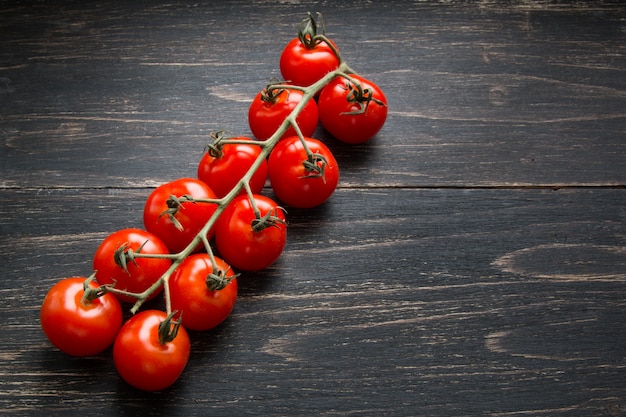 Tomates de cereza rojos en una rama en fondo oscuro. Dieta sana comida