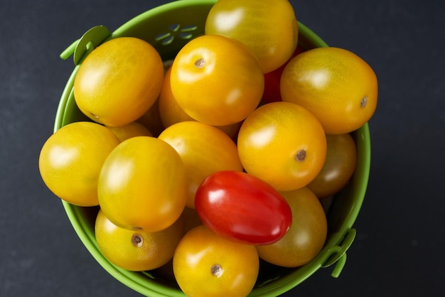 Tomates cherry amarillos en un mini cubo verde sobre un fondo oscuro.