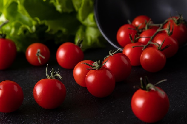 Los tomates cherry cayeron del plato. fondo oscuro decorado con hojas de ensalada