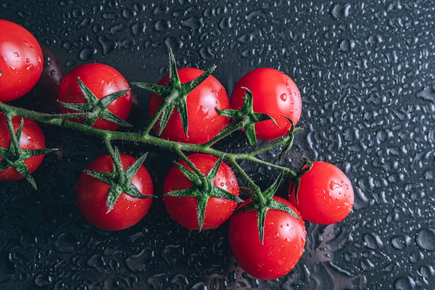 Tomates cherry cubiertos por gotas de agua aisladas en espacio negro