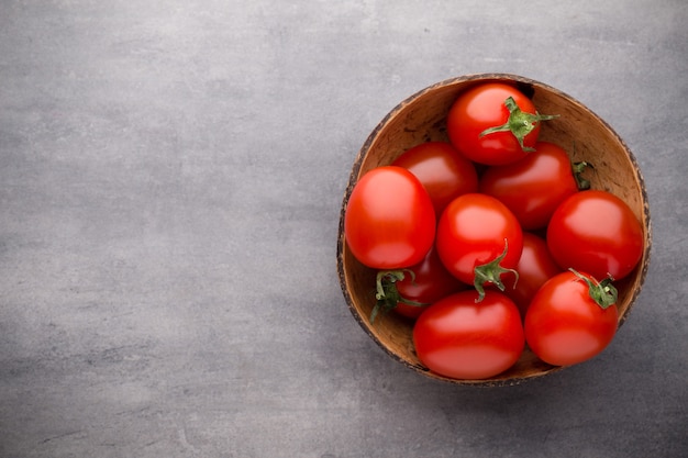 Tomates cherry en un cuenco de madera sobre un fondo gris