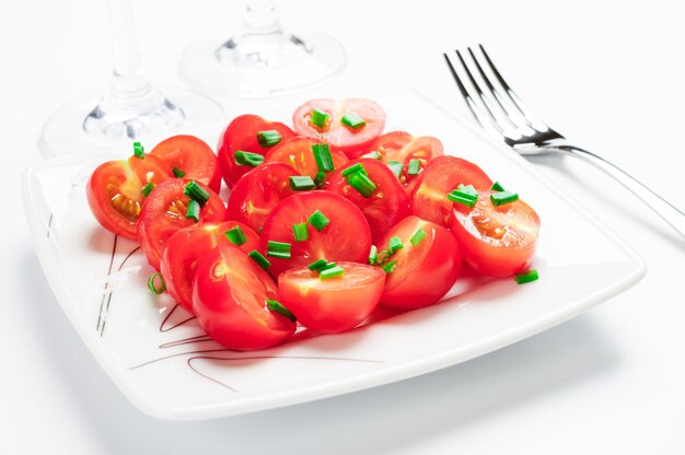 Tomates cherry decorados con cebollas verdes. En un plato cuadrado blanco.