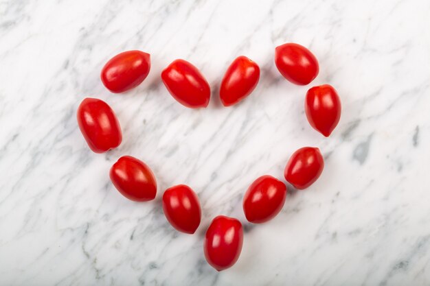 Tomates cherry dispuestos en forma de corazón sobre un fondo de mármol blanco