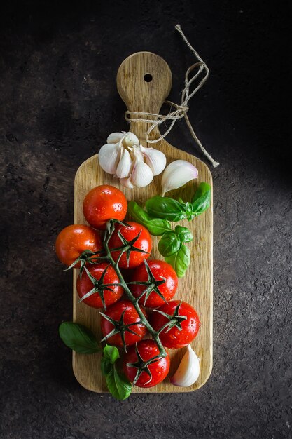 Tomates cherry ecológicos con albahaca y ajo sobre tabla para cortar