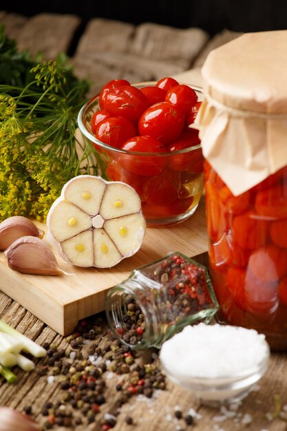 Tomates cherry enlatados en un frasco y un tazón de especias y hierbas sobre un fondo de madera