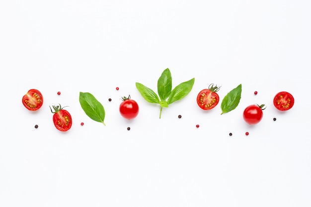 Tomates cherry frescos con hojas de albahaca y diferentes tipos de granos de pimienta en blanco Vista superior