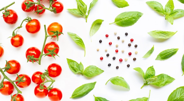 Tomates cherry frescos con hojas de albahaca y diferentes tipos de granos de pimienta.