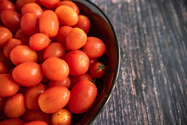 Tomates cherry frescos listos para servir en un plato negro sobre una mesa de madera