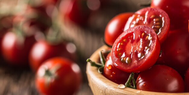 Tomates cherry frescos en un tazón de madera sobre la mesa de roble antiguo.