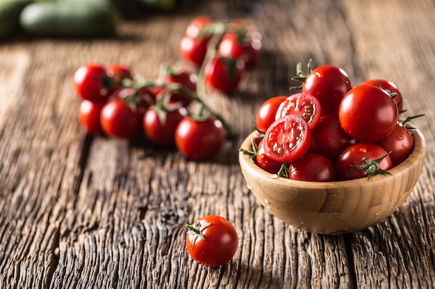 Tomates cherry frescos en un tazón de madera sobre la mesa de roble antiguo.