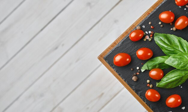 Tomates cherry con hojas de albahaca, sal y pimienta, diseño sobre una placa de piedra negra.