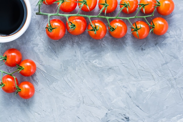 Tomates cherry maduros de miel en una rama y salsa balsámica en un tazón en gris concreto