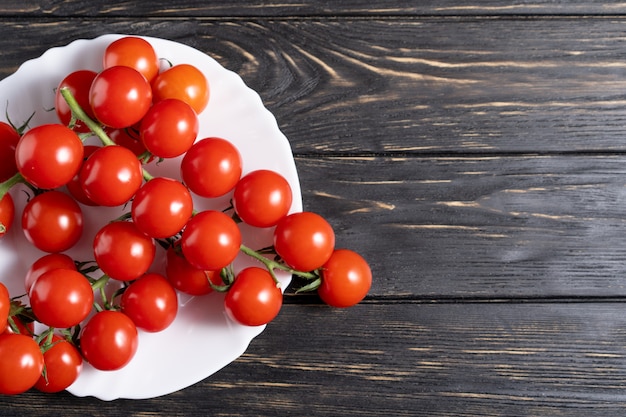 Tomates cherry en el plato blanco sobre la mesa de madera