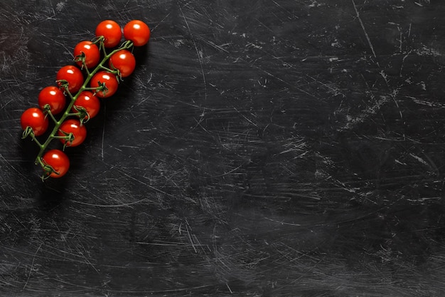 Tomates cherry, rama roja sobre fondo oscuro, con espacio para copiar texto, vista superior.