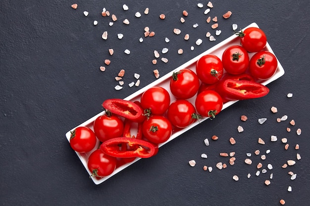 Tomates cherry recién lavados y rodajas de paprika en un plato oblongo blanco con sal rosa en una mesa de hormigón negro