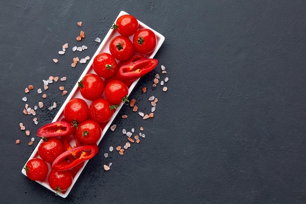 Tomates cherry recién lavados y rodajas de pimentón en un plato oblongo blanco con sal rosa y gotas de agua