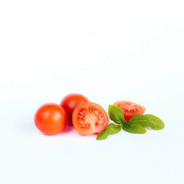 Tomates cherry rojos con albahaca verde sobre un fondo blanco. Foto de alta calidad