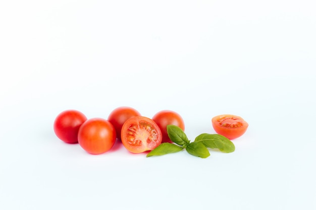 Tomates cherry rojos con albahaca verde sobre una superficie blanca.