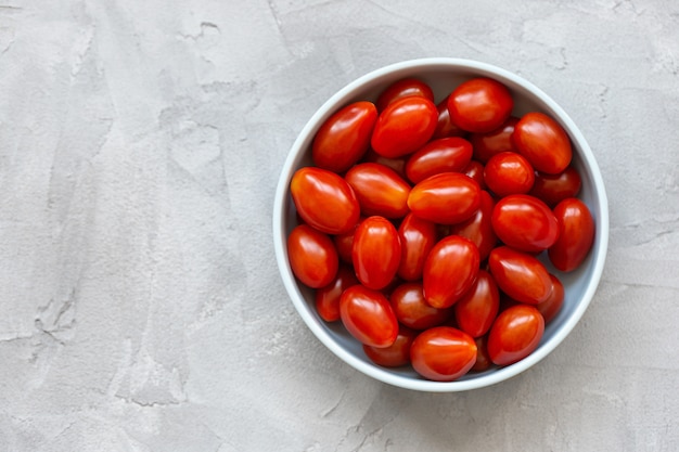 Tomates cherry rojos frescos en un recipiente en la pared de luz. Enfoque selectivo, copia espacio